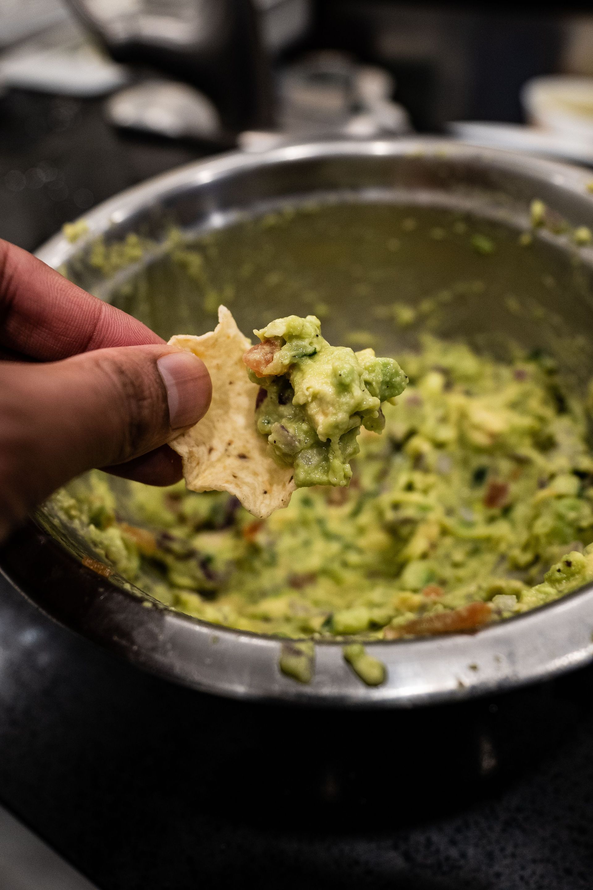 Close-up of a hand holding a tortilla chip dipped in fresh guacamole.